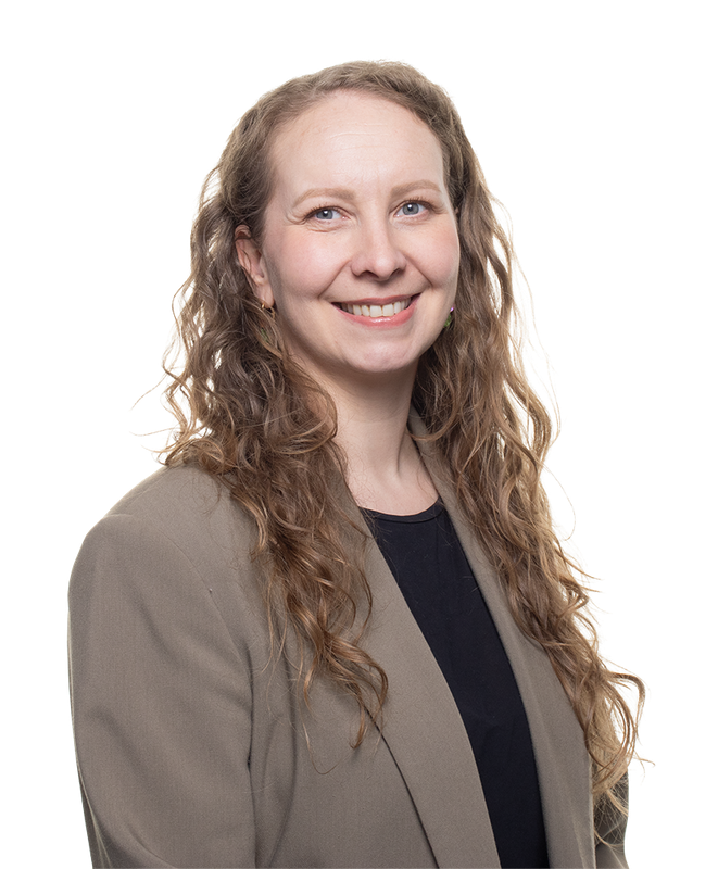 Nainen katsoo kameraan ja hymyilee iloisesti. Hänellä on pitkät kiharat hiukset ja jakkutakki.